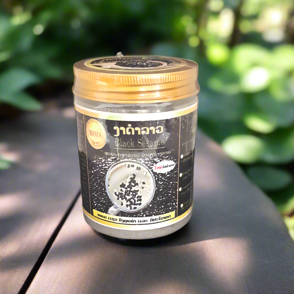 A container of Black Sesame Powder by Black Sesame Lao placed on a wooden surface with green leaves in the background.