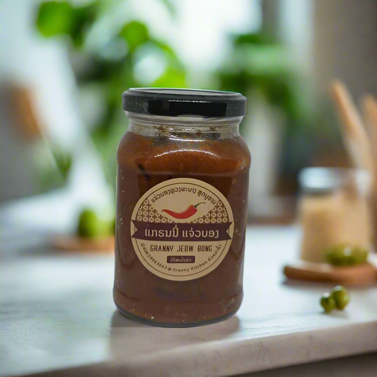 A 350g glass jar of Granny's Jeow Bong, an authentic Lao spicy chili paste, with a label displaying the product name and an image of chili peppers. The jar is placed on a kitchen counter with a blurred background.