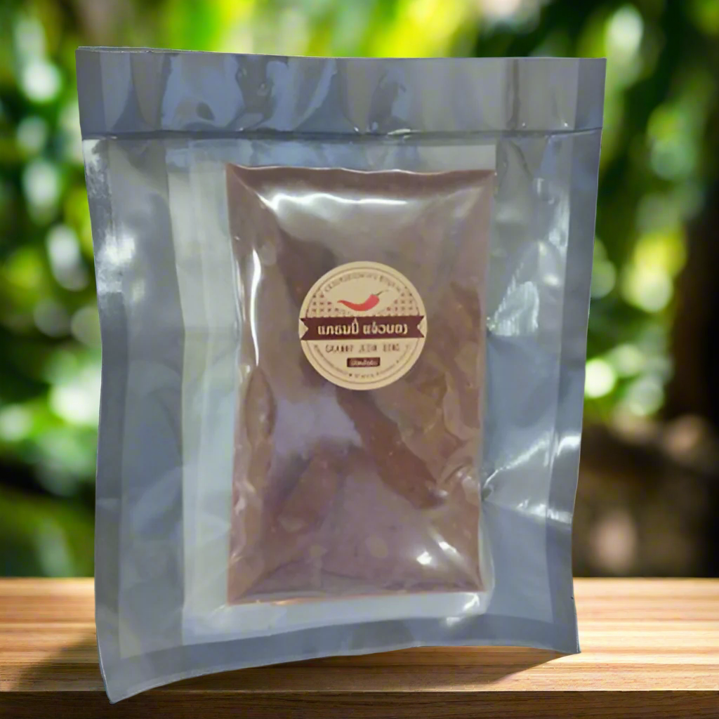 A vacuum-sealed bag containing Granny Jeow Bong, a type of Lao chili paste, placed on a wooden surface with a blurred green background.