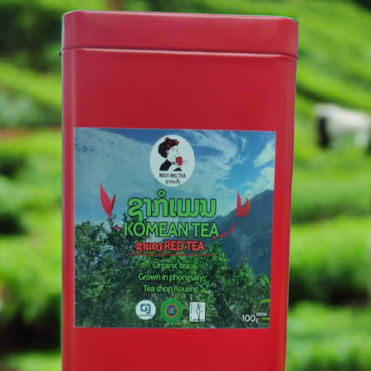 A red metal box of Komean loose leaf tea with a label depicting a tea plantation and the brand logo.