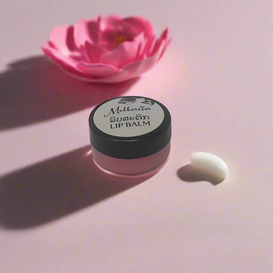 A small, open container of Mulberries Lip Balm on a pink background with a flower, suggesting a nourishing and natural lip care product.