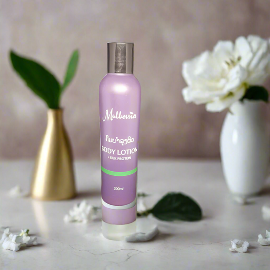 A bottle of Mulberries All Natural Body Lotion with Silk Protein, in a purple label, placed on a marble surface with a white vase and green leaves in the background.
