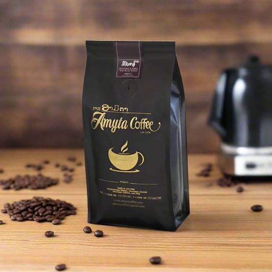 A package of Amyta Coffee Strong Robusta placed on a wooden surface with a coffee maker in the background and coffee beans scattered around.