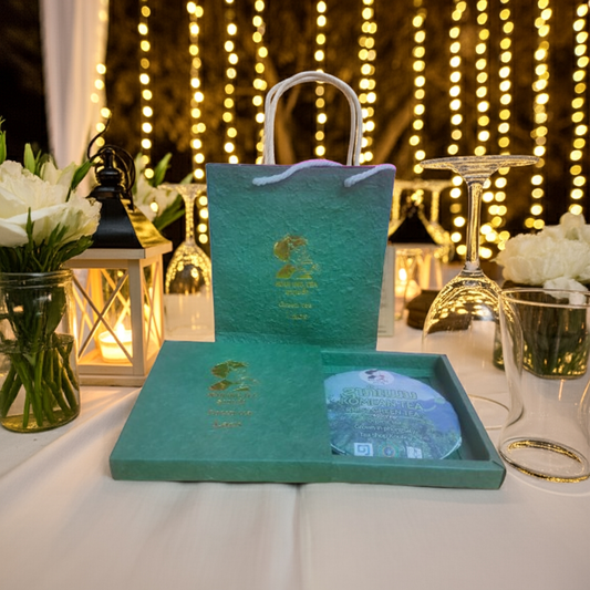 Green box with a lid featuring a logo on a table with decorative lights and flowers in the background