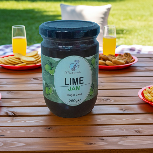 Jar of lime jam on a wooden table with snacks and drinks in the background